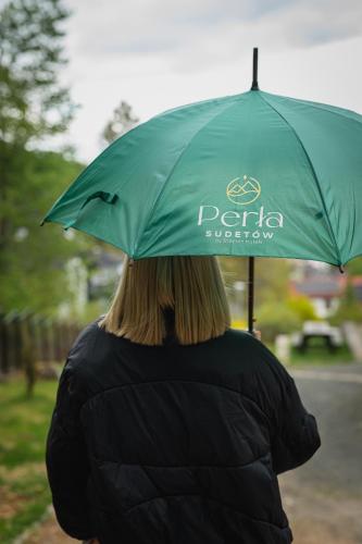 a woman holding a green umbrella in the rain at Perła Sudetów by Stay inn Hotels in Karpacz