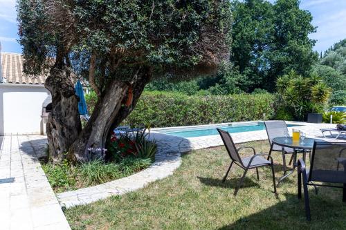 a table and chairs next to a tree next to a pool at Charmante petite maison à Corfou in Pelekas