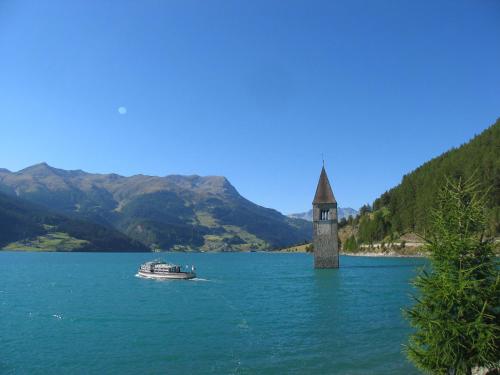 a boat in the middle of a lake with a clock tower at Vital Hotel Ortlerspitz in San Valentino alla Muta