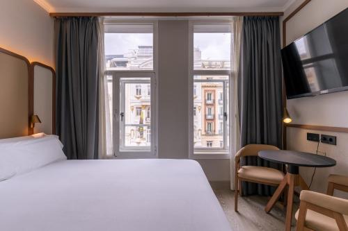 a hotel room with a bed and a desk and windows at Petit Palace Alcalá in Madrid