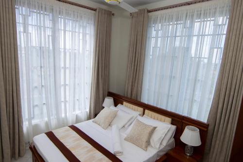 a bedroom with a bed with white pillows and windows at JJC BNB Mbweni in Bunju