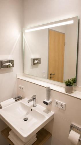 a white bathroom with a sink and a mirror at Hotel Artrium am Park in Dietzenbach