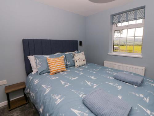 a bedroom with a bed with blue sheets and a window at Rosemary Cottage 2 in Tywyn
