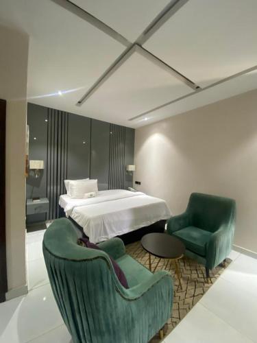 a bedroom with a bed and two green chairs at Wesley Hotels in Benin City
