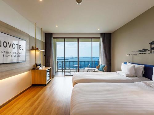 a hotel room with two beds and a balcony at Novotel Koh Si Chang in Ban Phanu Rangsi