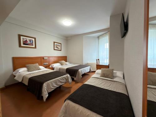 a hotel room with three beds and a tv at Hostal Restaurante Iruñako in Burgos
