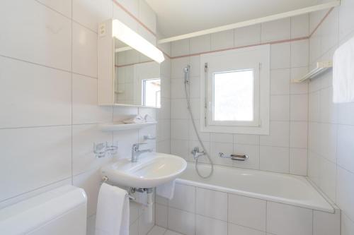 a white bathroom with a sink and a bath tub at Chesa Cravunera 29 in Sils Maria
