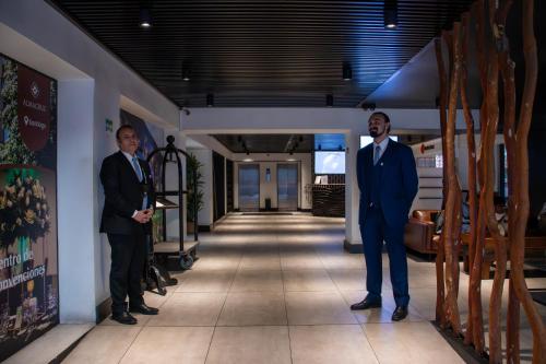 two men in suits are standing in a hallway at Almacruz Hotel y Centro de Convenciones (Ex Galerías) in Santiago