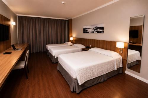 a hotel room with two beds and a desk at Kennedy Executive Hotel in São José