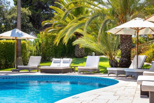 a pool with chairs and umbrellas next to a palm tree at Vila Balaia - Luxury Boutique Villas in Albufeira