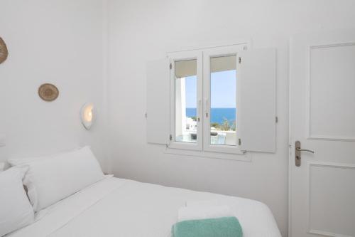 a white bedroom with a bed and a window at Red Beach Harmony suites Modestos in Akrotiri