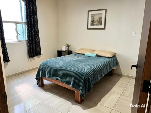 a bedroom with a bed with a blue comforter and a window at Mi Casa Morelia in Morelia