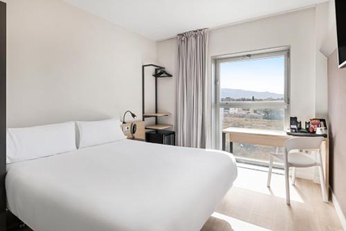 ein weißes Schlafzimmer mit Bett, Schreibtisch und Fenster in der Unterkunft B&B HOTEL Granada in Pulianas