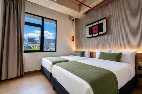 two beds in a hotel room with a window at Hunters Hotel Medellin in Medellín
