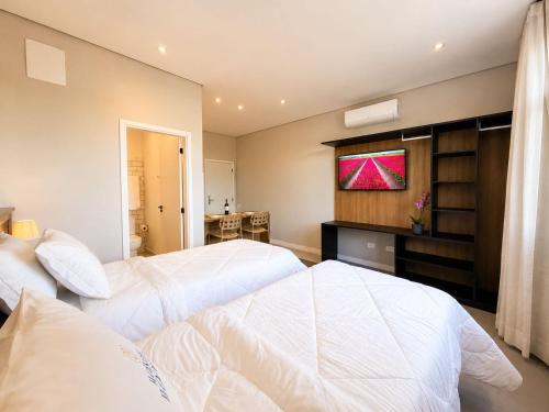 a bedroom with two beds and a television on the wall at Welkom Woord - Aluguel Flats e Aptos curta temporada - Entrada com senha in Holambra