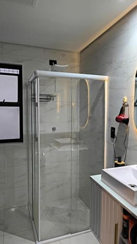a glass shower in a bathroom with a sink at Flat São Vicente Praia Piscina Garagem in São Vicente
