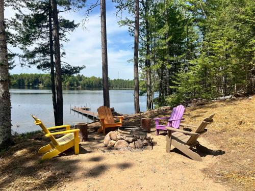 a group of chairs sitting around a campfire near a lake at Towering Pines Cottage in Saint Germain