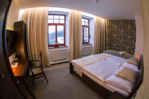 a bedroom with a bed and a desk and windows at Hotel Slunný Dvůr in Jeseník