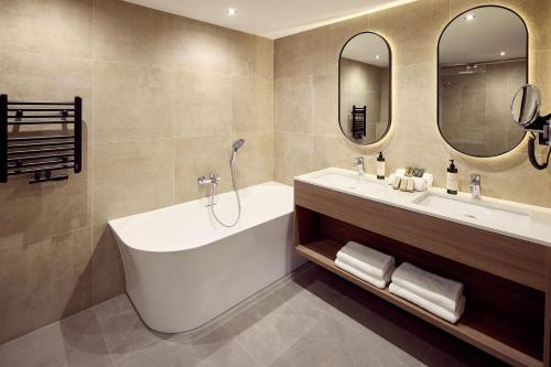 a bathroom with a tub and a sink and mirrors at Hotel Gladbeck van der Valk in Gladbeck