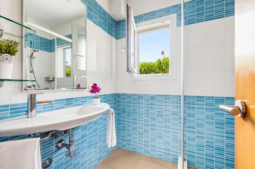 a blue tiled bathroom with a sink and a window at Villa Verano in Cala Galdana