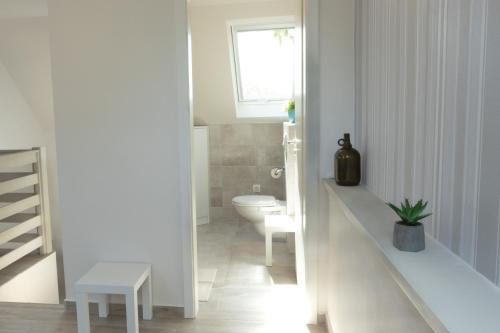 a white bathroom with a toilet and a window at Kardos Villa in Szigliget