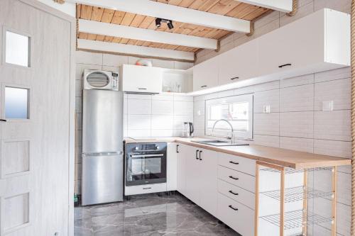 a kitchen with white cabinets and a stainless steel refrigerator at Domki Anchor - Rodzinne Domki - Cisza i Spokój in Lubiatowo