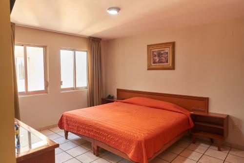 ein Schlafzimmer mit einem Bett mit einer orangefarbenen Decke in der Unterkunft Hotel Real Alteño in Tepatitlán
