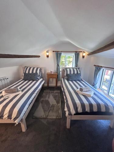 two beds in a room with two windows at Forge Cottage in Polperro