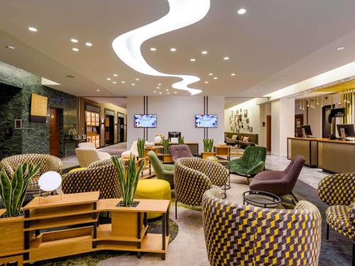 a hotel lobby with chairs and tables and televisions at Hotel Mondial am Dom Cologne MGallery in Cologne