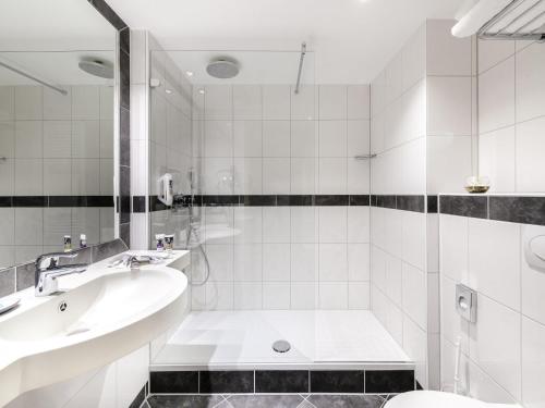 a white bathroom with a tub and a sink at Mercure Hotel Saarbrücken City in Saarbrücken