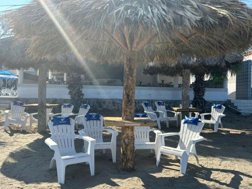 a group of white chairs and a table with a straw umbrella at PELÍCANOS Hotel & Beach Club in El Zapote