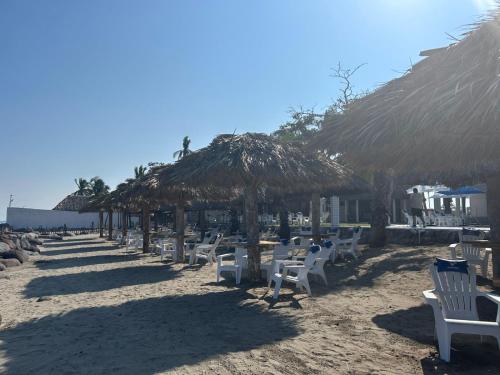 a row of chairs and straw umbrellas on a beach at PELÍCANOS Hotel & Beach Club in El Zapote