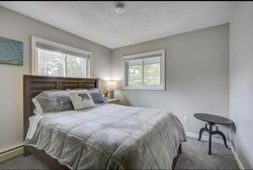 a bedroom with a bed with a table and two windows at Central White Mountains Retreat in Bartlett