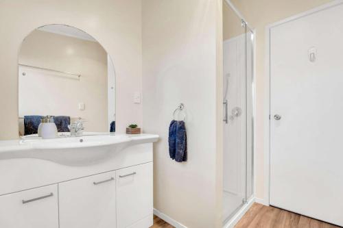 a white bathroom with a sink and a shower at Fun on the Fairway in Matarangi