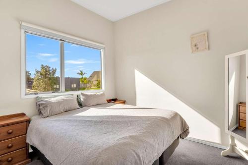 a bedroom with a bed and a large window at Fun on the Fairway in Matarangi