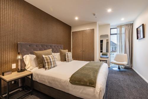 a bedroom with a large bed and a chair at Quest Queenstown Apartments Remarkables Park in Queenstown