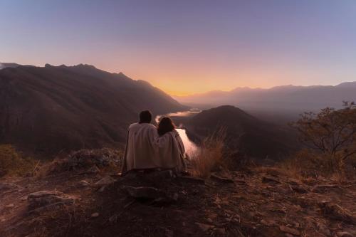 a couple sitting on top of a mountain watching the sunset at Sentio Camps - All Inclusive in Cabra Corral