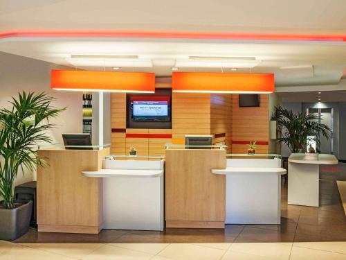 an office lobby with a reception counter with orange lights at Ibis Cornella in Cornellà de Llobregat