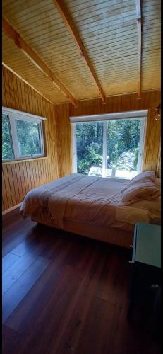 a large bed in a wooden room with windows at Entre Bosque Puelo in Puelo