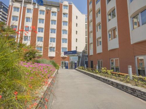 a walkway in front of a building with pink flowers at Novotel Salerno Est Arechi in Salerno