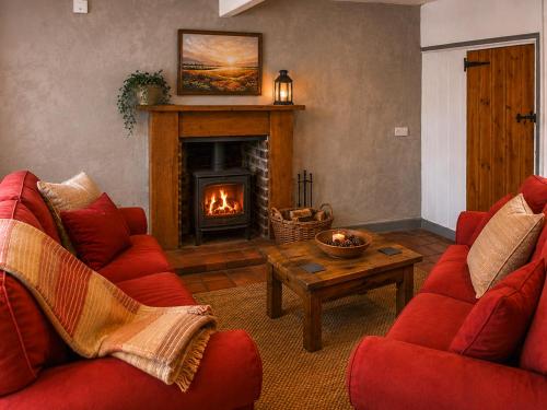 a living room with two red chairs and a fireplace at Mark's Cottage in North Walsham