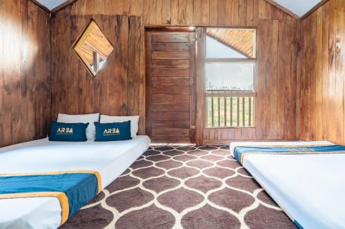 two beds in a room with wooden walls and a window at RB Cottage Resort By ARBA in Palayangan