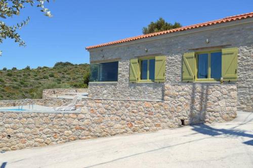 a stone house with green shutters and a stone wall at Villa Rokanes Glass Stone with Pool in Kouvéllai