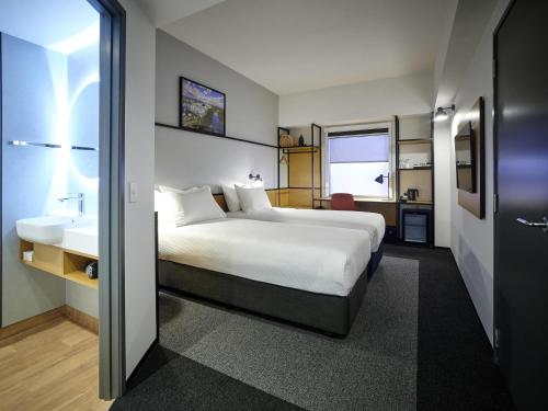 a bedroom with a large white bed and a bathroom at ibis Hamilton Tainui in Hamilton