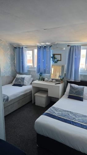 a bedroom with two beds and a desk and blue curtains at Glendor Hotel in Blackpool
