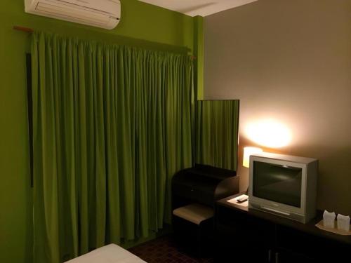 a hotel room with green curtains and a television at Baan Chomphu in Prachuap Khiri Khan