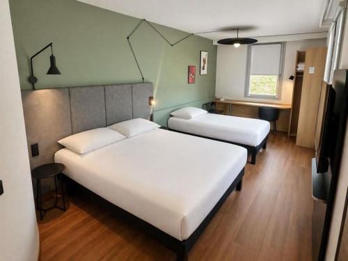 a bedroom with two beds and a table and a window at ibis Beauvais Aéroport in Beauvais
