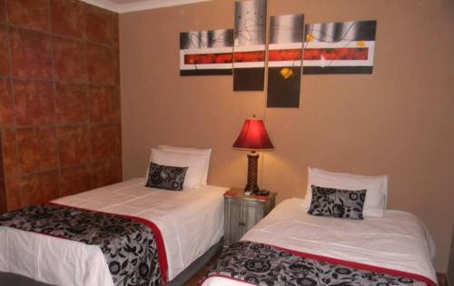 two beds in a hotel room with a lamp and a lamp at La Postma House in Postmasburg