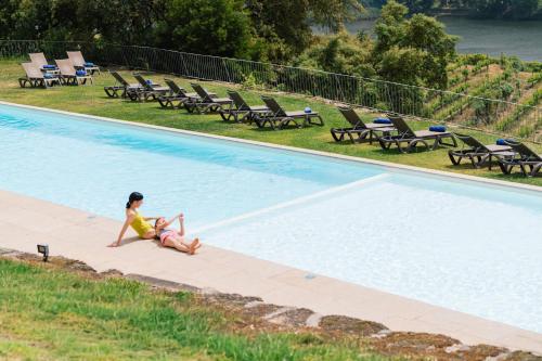 a woman sitting on the edge of a swimming pool at Douro Palace Hotel Resort & SPA in Baião