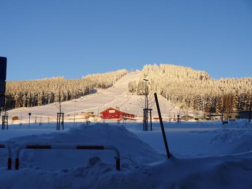 a snow covered hill with a red building in the distance at Ferienwohnung Schneemann in Hohegeiß